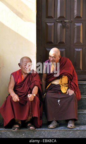two old monks on the stairs in front of an entrance in Swayambhunath, an ancient religious complex atop a hill west of the city, Nepal, Kathmandu Stock Photo