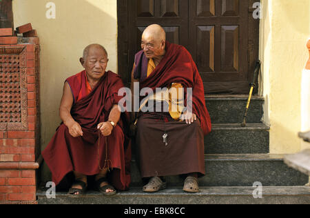 two old monks on the stairs in front of an entrance in Swayambhunath, an ancient religious complex atop a hill west of the city, Nepal, Kathmandu Stock Photo