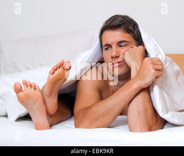 young couple lying frustrated under the bed spread Stock Photo