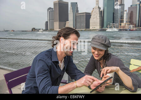 USA, New York State, New York City, Brooklyn, Happy couple sitting and using tablet pc with cityscape in background