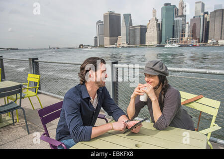 USA New York State New York City Brooklyn Happy couple sitting and using tablet pc and drinking coffee cityscape in background