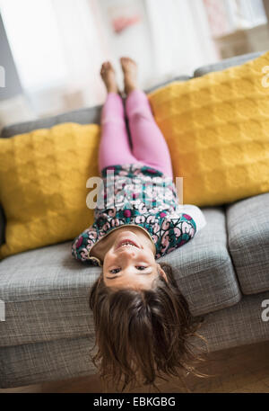 Girl (6-7) lying upside down on sofa Stock Photo