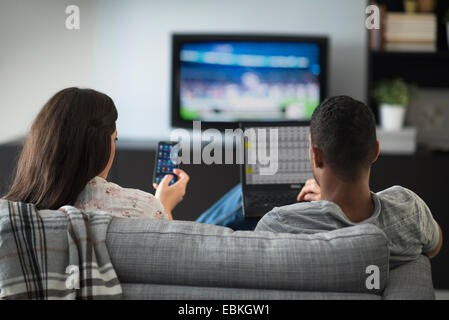 Couple sitting in living room, using laptop and cell phone Stock Photo