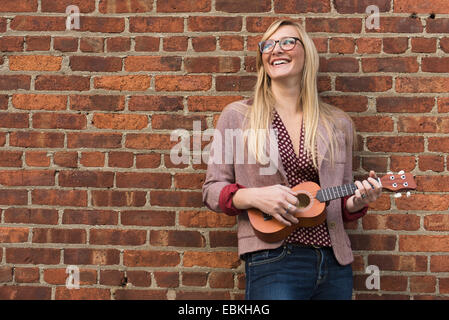 Woman standing against brick wall and playing ukulele Stock Photo