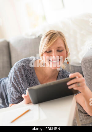 Smiling woman lying down on sofa with tablet pc Stock Photo