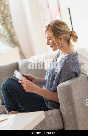 Pensive woman sitting on sofa with tablet pc Stock Photo