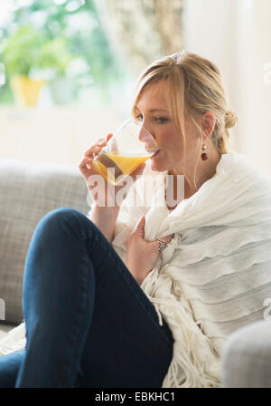 Woman sitting on sofa and drinking orange juice Stock Photo