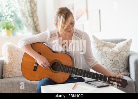 Woman sitting on sofa and playing acoustic guitar Stock Photo