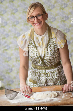 Smiling woman using rolling pin while kneading dough Stock Photo