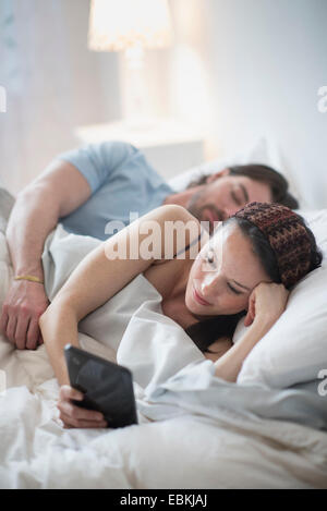Couple in bed, woman reading on digital tablet and man sleeping Stock Photo