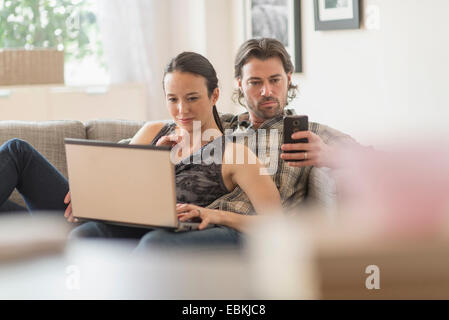Couple on sofa, woman using laptop and man mobile phone Stock Photo