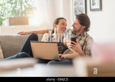 Cheerful couple on sofa with laptop and mobile phone