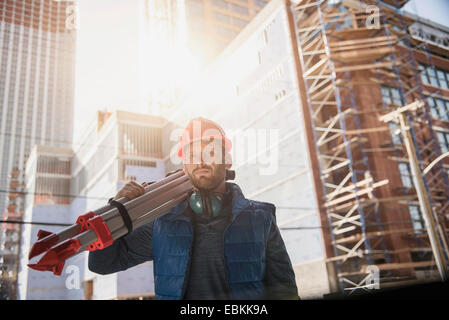 Construction worker carrying tripod on shoulder Stock Photo