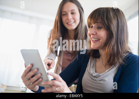 Teenage girl (14-15) using digital tablet with her mom in living room Stock Photo