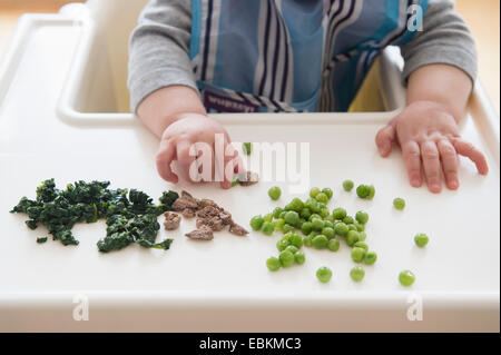 Baby girl (12-17 months) eating steak, spinach and green peas Stock Photo