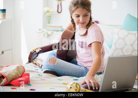Girl (12-13) playing guitar and using laptop Stock Photo