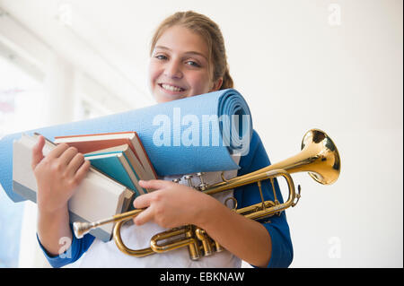 Portrait of teenage girl (12-13) holding rolled-up exercise mat, books, and trumpet