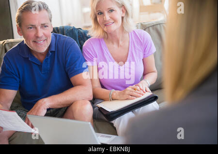 Portrait of couple sitting on sofa smiling at woman in blurred foreground Stock Photo