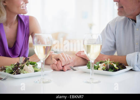 Cropped view of couple holding hands in restaurant with glasses of white wine in foreground