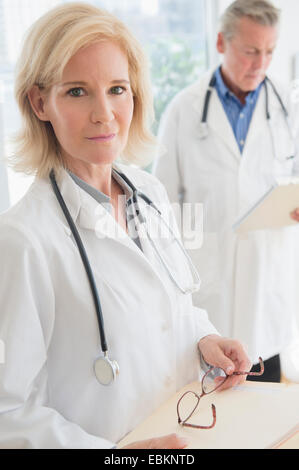 Portrait of female doctor holding clipboard and eyeglasses Stock Photo
