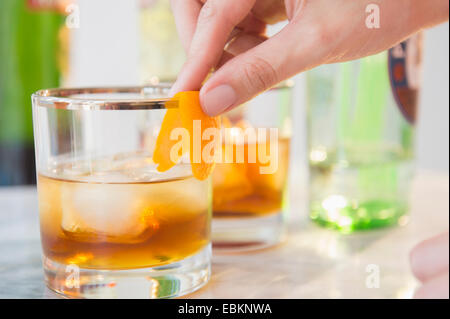 Close-up shot of bartender's hand decorating cocktail glass with orange peel Stock Photo