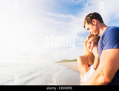 USA, Florida, Jupiter, Portrait of young couple embracing on sandy beach, against background of coastline Stock Photo