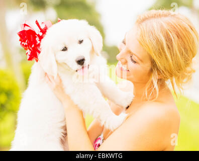 USA, Florida, Jupiter, Young woman holding white puppy with ribbon bow Stock Photo