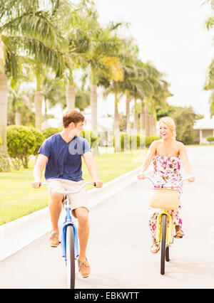 USA, Florida, Jupiter, Young couple driving bicycles along street with palm trees Stock Photo