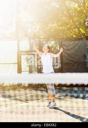 USA, Florida, Jupiter, Young woman in tennis court about to serve ball with net in blurred foreground Stock Photo