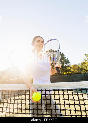USA, Florida, Jupiter, Portrait of young woman standing by net, holding tennis ball and tennis racket Stock Photo