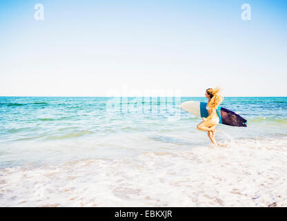 USA, Florida, Jupiter, Young woman running in surf into sea carrying surfboard Stock Photo