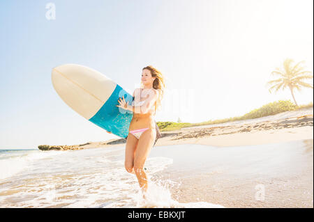 USA, Florida, Jupiter, Young woman running in surf into sea carrying surfboard Stock Photo