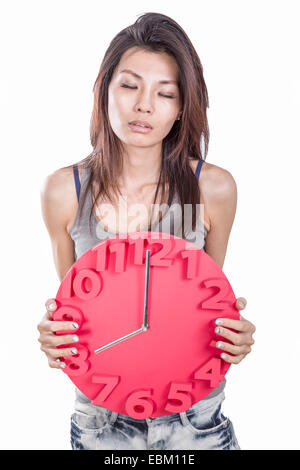 Chinese woman looking tired holding clock showing eight o' clock; conceptual late for work or meeting Stock Photo