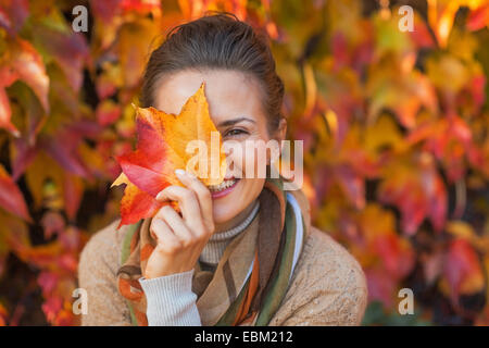 Portrait of happy young woman hiding behind autumn leafs in front of foliage Stock Photo