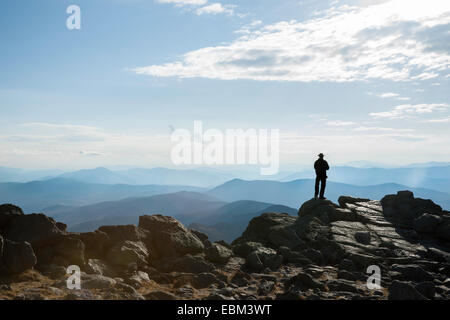 Unrecognisable silhouette of man standing on rock ledge in distance, at summit of Mount Washington, looking out over the vista Stock Photo