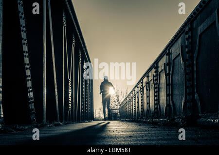 Jogger on riveted steel railway bridge at sunrise Stock Photo