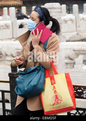 Chinese woman using smartphone while wearing a pollution mask because of heavy smog - coronavirus corona virus Stock Photo