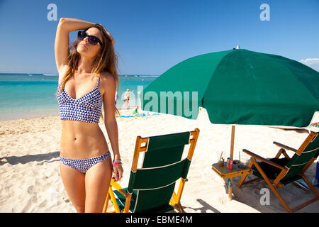 Attractive woman standing on beach in bikini near beach umbrella Stock Photo