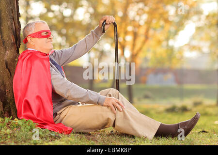 Senile old man sitting outdoor in a superhero costume Stock Photo