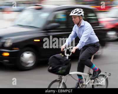 London, UK - October 23, 2014: A commuter cyclist wearing shirt and cufflinks negotiating the traffic of buses cars and taxis in Stock Photo