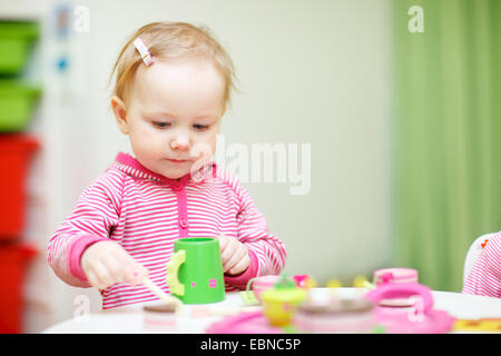 little girl plays drink coffee with plastic toys Stock Photo
