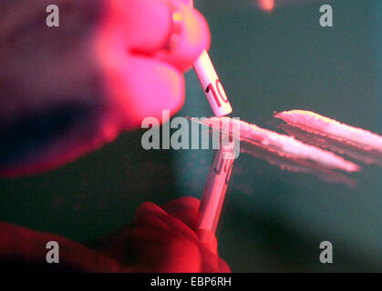 hand of a drug consumer having prepared two cocaine lines on the table to snort them through a rolled 10 Euro bill Stock Photo