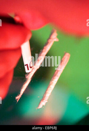 drug consumer snorting through a rolled 10 Euro bill two cocaine lines prepared on the table Stock Photo
