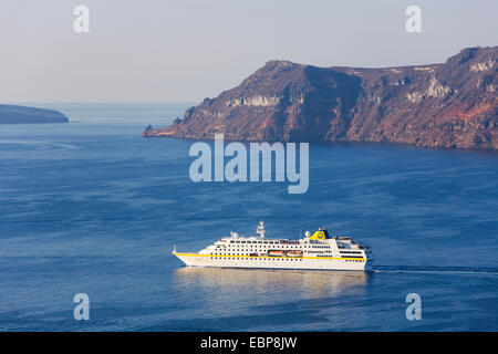 Ia, Santorini, South Aegean, Greece. Cruise ship crossing the caldera beneath the deep red cliffs of the island of Thirasia. Stock Photo