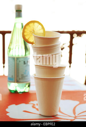 stacked disposable cups with a lemon wedge with a bottle of water on a orange place mat natural light Stock Photo