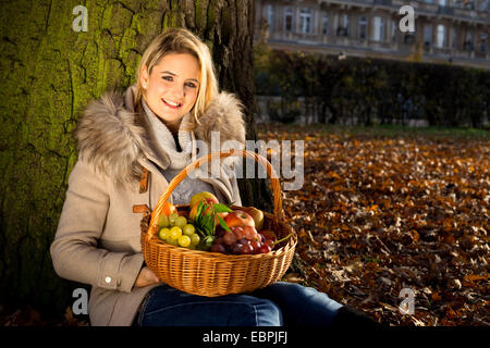 young woman holding a basket full of fruits in a park during autumn Stock Photo