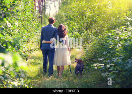 Young hugging newlyweds walking with dog in the forest back to camera Stock Photo