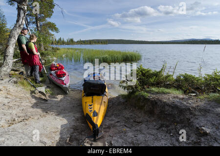 couple standing next to kayaks at the lakeshore and looking to Rogen lake, Sweden, Haerjedalen, Naturreservat Rogen Stock Photo