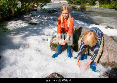 two children holding ice from glacial river in their hands , Norway, Jostedalsbreen National Park, Supphella Stock Photo