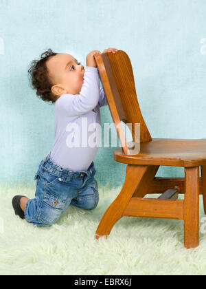 Adorable African baby boy trying to stand with help of a chair Stock Photo